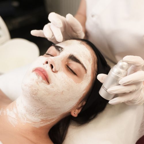 Doctor cosmetologist makes a nourishing mask for face and holding a jar of cream in his hands